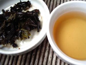 A cup of oolong tea with a golden color, and used tea leaves on the left