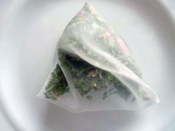 Pyramid-shaped tea bag filled with fine pieces of green leaves and lavender flowers