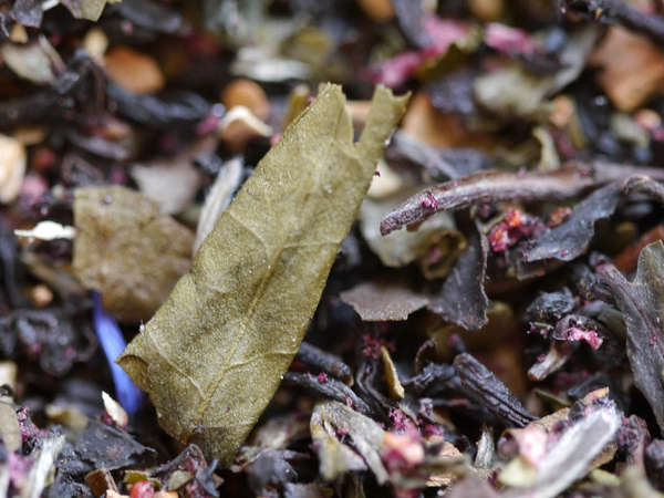 Colorful loose-leaf flavored tea blend with black tea leaves, blue and purple flowers, and large olive-green dried leaves