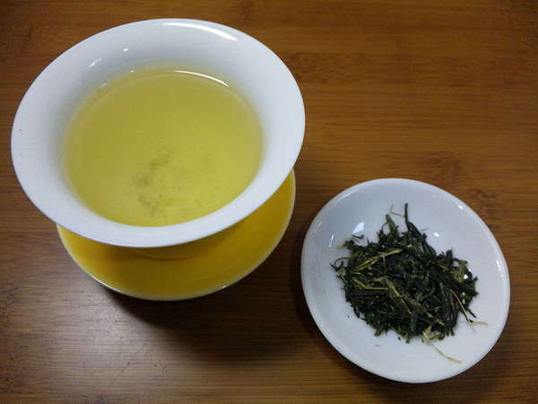 Brewed cup of tea with golden-green color top left, dish with dark green loose-leaf tea lower right