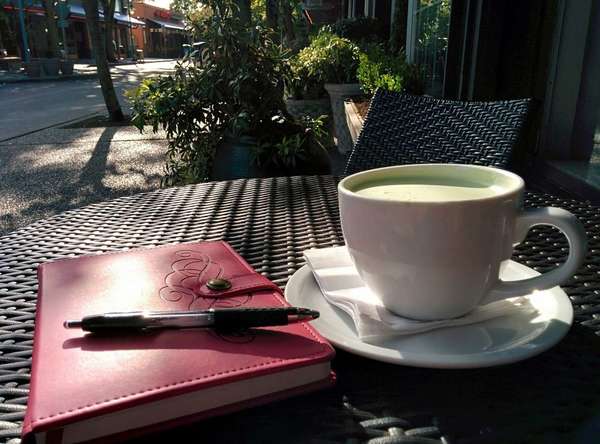 Closed journal with pen on top, cup of foamy green tea, on table along a street
