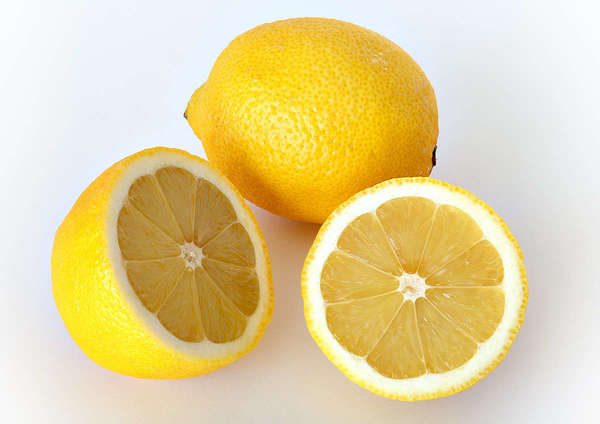 Two lemons, one whole, one sliced showing two cross-sections, on a white background