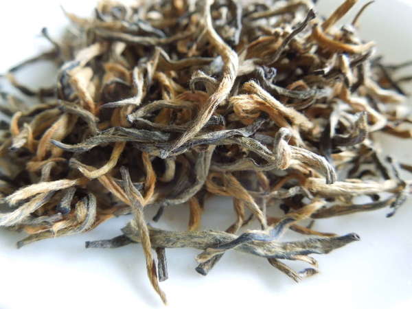 Loose-leaf Tea with golden-orange and gray-black twisted, hairy leaves