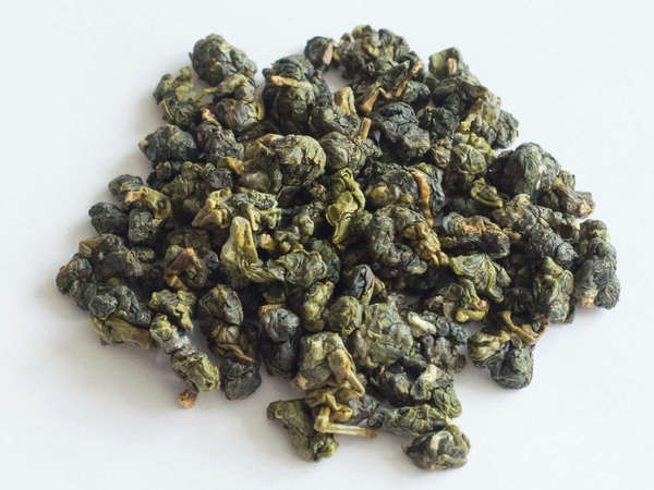 Tightly-rolled oolong tea leaves, bright green with golden and dark green accents, on white background