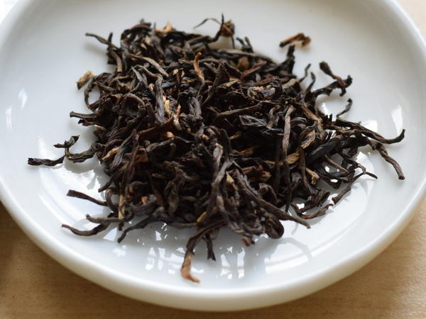 Wiry, crinkly black tea leaves with golden tips, in a white dish