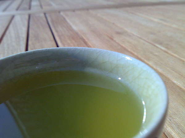 Bright green tea in ceramic cup, on wooded table with slats